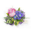 A delicately composed corsage or boutonnière set against a crisp white studio background, lovingly arranged to read as both modern and romantic. At its heart sits a single rose, petals unfurling from a soft lavender-pink core that graduates outward to a lively fuchsia rim, the velvety surface catching a soft, diffused light that hints at the rose's gentle fragrance. Beside it, a compact spray of indigo-purple florets - hydrangea-like in form - offers a jewel-toned contrast; each tiny blossom holds a bright blue and lime-green center that seems to glow against the deeper petals. The blooms are cradled by a thoughtful mix of foliage: broad variegated ivy leaves with deep emerald centers and sunny yellow margins give classic structure, while silvery-green, slightly fuzzy leaves (suggestive of lavender foliage) soften the silhouette. A sculptural, striped green-and-cream leaf curls through the composition, adding movement, and fine, airy sprigs of asparagus-fern provide a feathered, breathy texture. Underpinning the cluster, an intricate dark purple mesh peeks from beneath, creating modern depth and a subtle sparkle that lifts the colours. To the lower right, a short strand of lustrous white pearls is visible - delicate evidence of a wristlet or lapel attachment and a nod to tradition. Compact and meticulously balanced, this piece feels suited to weddings, proms, or milestone celebrations; it reads both timeless and contemporary, the kind of small floral keepsake one might carry from a ceremony on Clerkenwell Green to a reception near Exmouth Market.