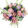 Set against a pure white background, this hand-tied bouquet feels like a moment of calm luxury, as if it has just left a studio near Exmouth Market and is pausing in stillness before being carried through Clerkenwell's cobbled streets. At its heart, generous garden roses in blush pink, dusty mauve, and antique rose unfurl in layered spirals, their velvety petals forming a soft, romantic core that suggests affection and care. Around them, plush carnations add a billowing texture; each petal shifts from a pale, creamy centre to more saturated blush and plum-rose edges, creating a delicate, frilled halo of colour. Punctuating these gentle tones, deep indigo and royal blue blooms stand out, including a striking royal blue anemone with a near-black centre that commands attention near the lower front of the bouquet. Some of the blue flowers remain as smooth, tulip-like buds, adding structure and a sense of unfolding life. Slender wands of lilac and pale lavender stock thread upward, their small clustered flowers adding fragrance and a fluttering, vertical lightness that keeps the bouquet feeling open and airy. Encircling and weaving through everything, dark green foliage and rounded, silvery eucalyptus leaves bring contrast and freshness, their cool tones hinting at a clean, herbal scent. The stems are neatly gathered and visible at the base, clearly tied by hand in a classic spiral. This arrangement radiates quiet elegance and reassurance, perfect for an anniversary surprise, a thoughtful thinking of you, or a graceful display in a Clerkenwell home overlooking one of the area's hidden garden squares.