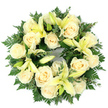Viewed flat against a clean white backdrop, this circular sympathy wreath reads as a quiet promise of consolation: cream-coloured roses nestle in a dense ring, their tightly furled petals forming almost perfect rosettes, while soft pale yellow lilies arc gently between them, some fully open to reveal slender stamens and others kept shyly in bud. The composition is generously cushioned by deep green foliage - feathery fern fronds that supply a lacy, soft-edge texture and clusters of rounded, silvery-green leaves that suggest eucalyptus - each leaf adding cool depth so the pale blooms seem to glow. From a florist's hands the piece is balanced, symmetrical and deliberately full, with roughly a dozen to twenty large roses creating a soothing ivory field and the lemon-tinted lilies bringing restrained height and a graceful, trumpet-shaped silhouette. The scent is hinted at in the arrangement: the faint, powdery sweetness of roses with a green, almost citrus lift from the lilies, a gentle perfume suited to a funeral chapel or a quiet memorial space. The circular form reads as an emblem of unbroken remembrance, an offering that feels both dignified and intimate. As a local florist who has placed wreaths around Clerkenwell Green and delivered tributes near Exmouth Market and Spa Fields, I imagine this wreath laid softly at a service, its soft palette speaking of purity, peace and steady, enduring affection. The craftsmanship shows regard and restraint-an arrangement meant to comfort, to frame memory, and to convey sympathy without fuss, reflecting the thoughtful tone suited to a farewell or graveside tribute.