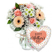 This Mother's Day arrangement is captured in a bright, minimalist setting, with a pure white background that lets the colours of the bouquet and balloon feel almost luminous. Centre-left in the frame stands a clear, gently contoured glass vase, filled with fresh water and neatly trimmed stems that reveal the careful craftsmanship of a local Clerkenwell florist. Rising from the vase is a lush, rounded bouquet in a palette of peach, pink, white, and leafy green. Several peach-pink roses are in full bloom, their layered petals forming soft spirals that draw the eye inward. Alongside them, cheerful peach gerbera daisies with dark, velvety brown centres radiate outward like little suns, bringing energy and joy to the design. Nestled between these focal flowers are clusters of white baby's breath, their tiny blossoms creating a delicate, cloud-like veil that softens the edges of the arrangement. Small white chrysanthemums, each with a hint of apple-green at the centre, add fullness and a crisp, daisy-fresh look. Glossy green foliage supports the pastel tones, offering contrast and a sense of garden vitality, much like the greenery found in Clerkenwell's hidden courtyards. Around the neck of the vase, a loop of rustic twine adds a touch of handmade warmth. To the right of the bouquet, a heart-shaped foil balloon leans in, its white surface dotted with metallic gold and silver confetti spots that shimmer under the light. At the balloon's centre sits a peach-coloured heart, framing the words HAPPY Mother's DAY in bold black script, with the word Mother's written in a particularly flowing, celebratory style. A small white greeting card peeks from behind, suggesting a personal message ready to accompany same-day Mother's Day deliveries across Clerkenwell and nearby creative districts.